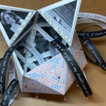 3D sculpture including pins and black and white photographs with quotes on strips of paper in all directions.