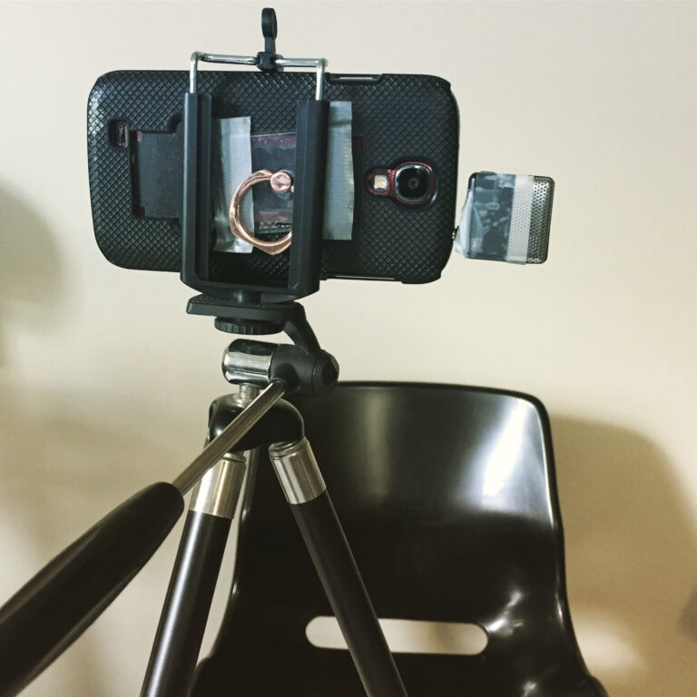 A photograph of a smartphone on a tripod with a microphone plugged into the auxiliary plug