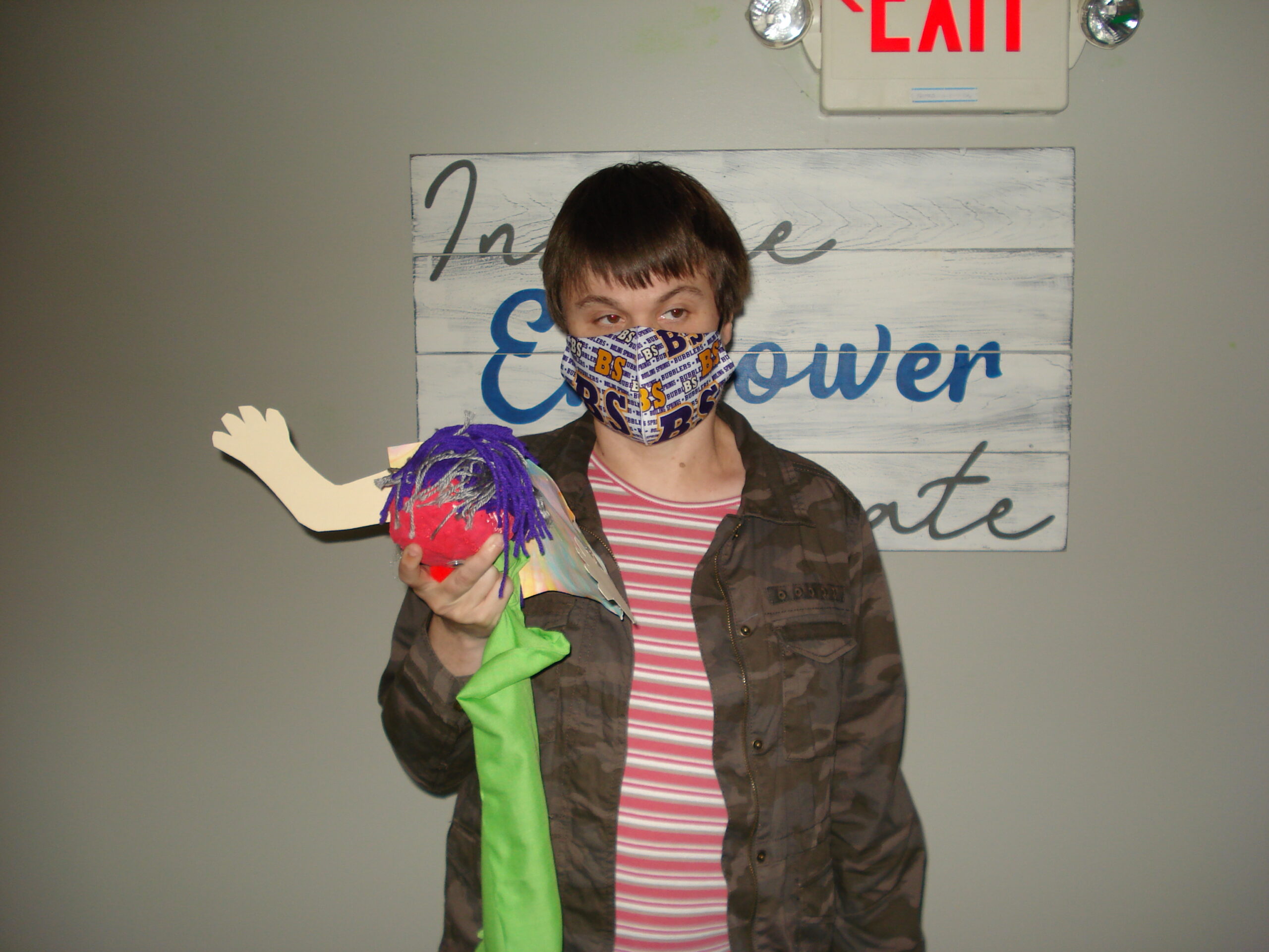 Photograph of a person holding a puppet that was made in an art class. the puppet has a green sleeve with a hand popping out of it