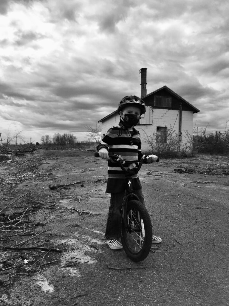 A young child riding on a bicycle with a house and clouds in the background